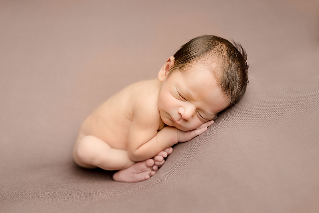 naked newborn baby on a brown backdrop sleeping