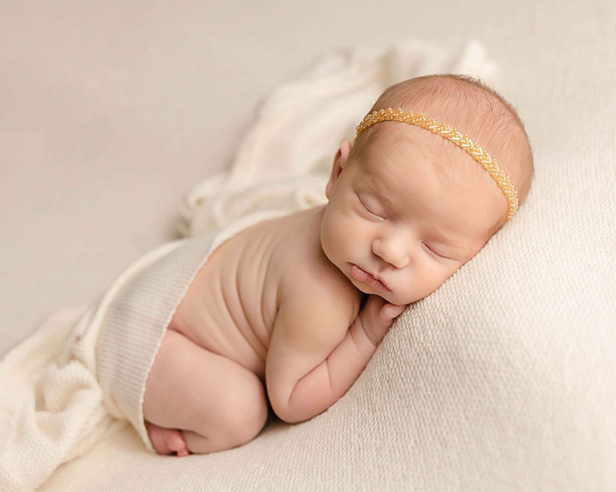 newborn baby girl in a neutral wrap laying on her hands