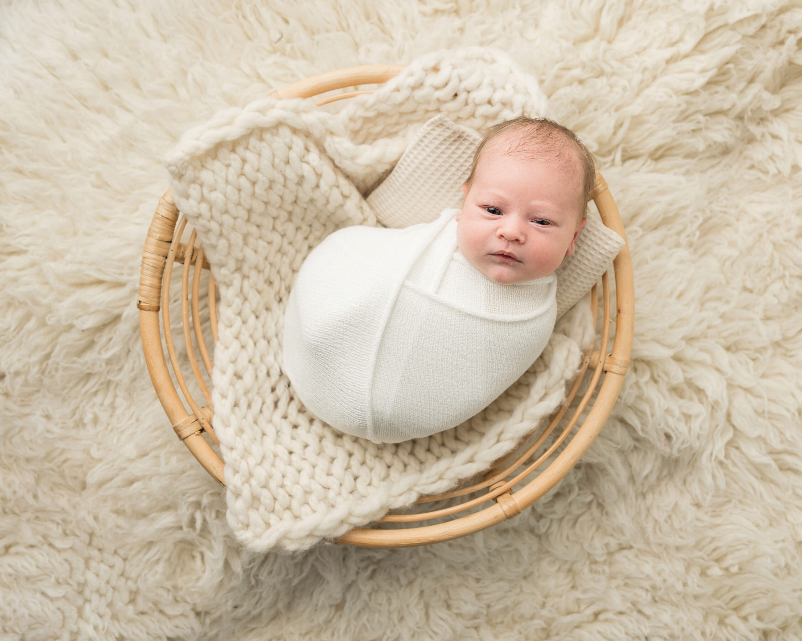 newborn baby wrapped in white laying in a large basket Baby Nest Birth Services