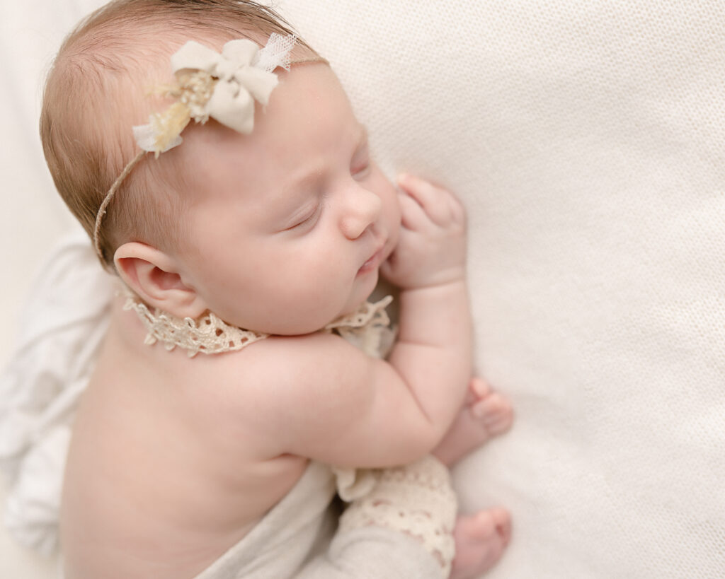 newborn baby with a cream headband sleeping on her hands Brave Birth Doulas