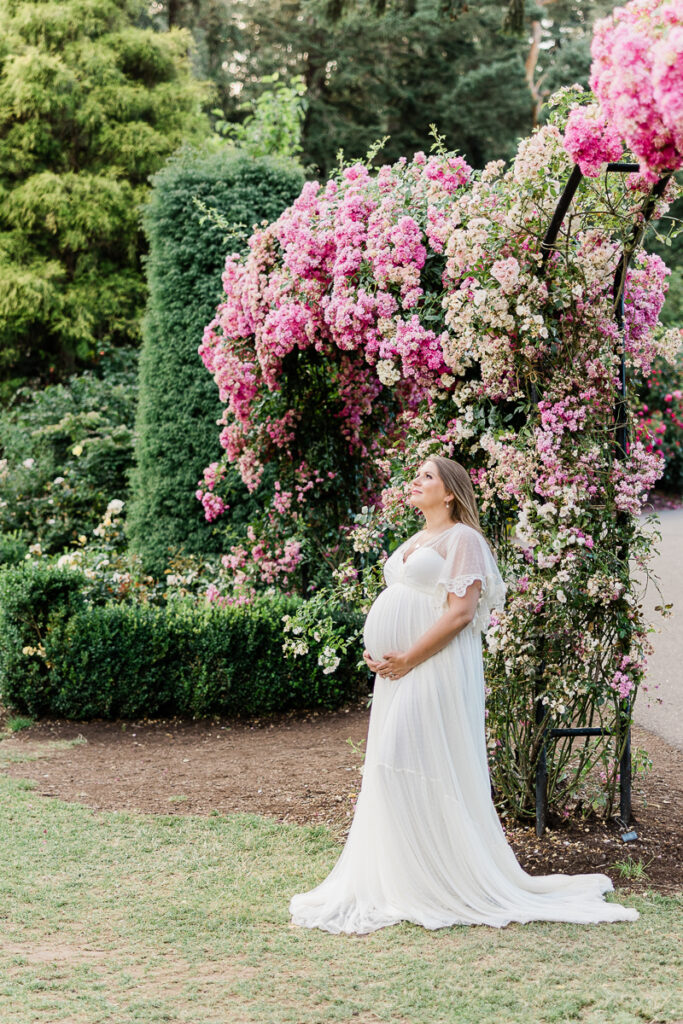 profile view of a mom in a white maternity gown holding her bump in a garden