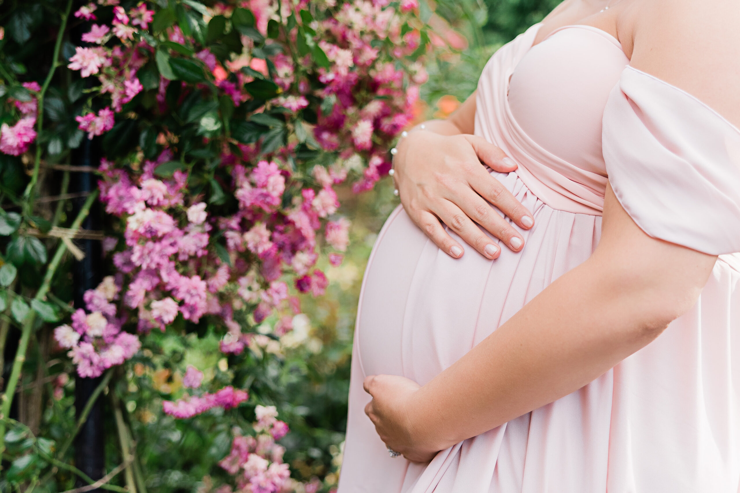 closeup of a baby bump near pink flowers Midwifery Birth Center Portland
