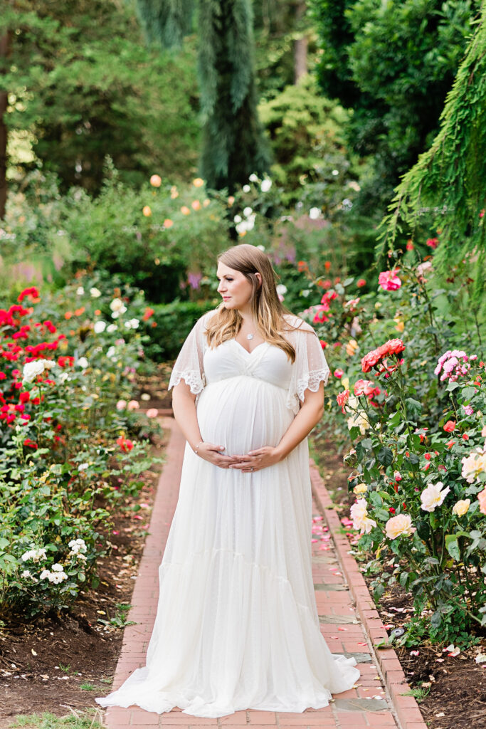 mom to be in white maternity gown standing in a garden of pink flowers Midwifery Birth Center Portland