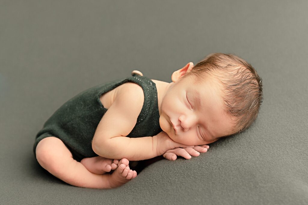 newborn baby boy in green sleeveless onesie sleeping on his hands Sweetpea’s Portland