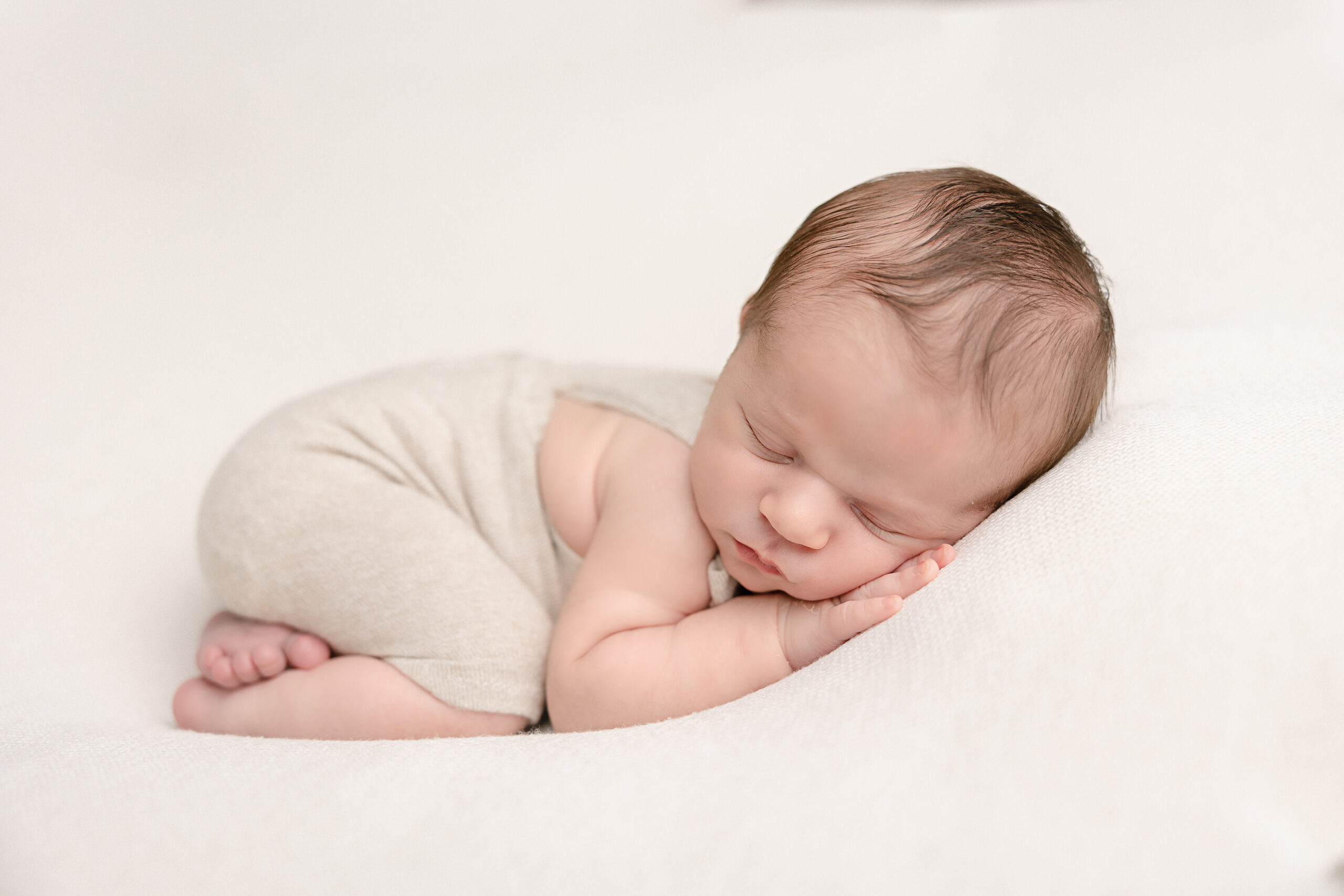 newborn baby in neutral clothing sleeping on his hands