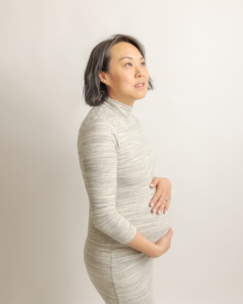 mom to be in grey maternity dress looking up at the sky while holding her bump