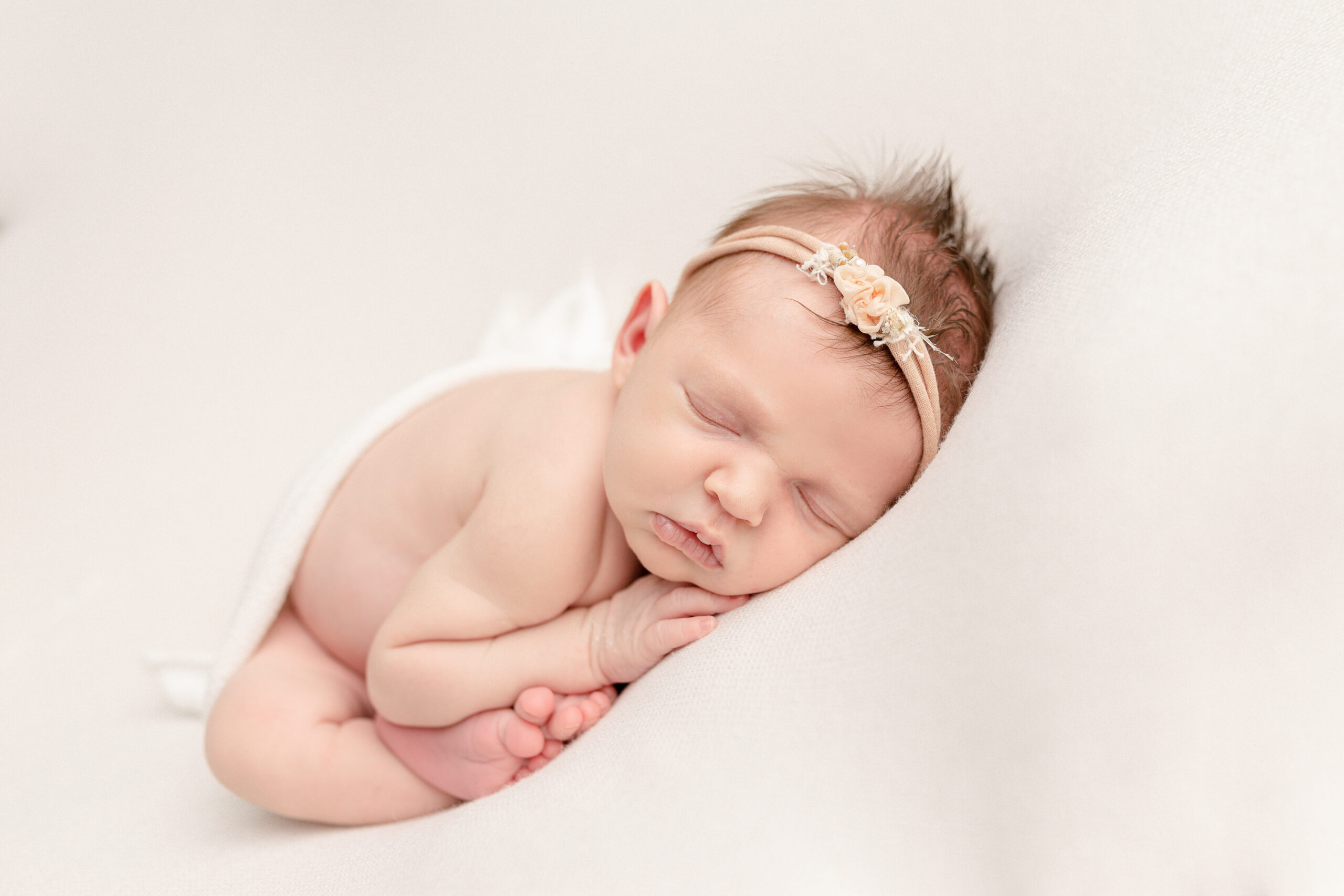 newborn baby girl with a white blanket and headband sleeping on her hands ABC Doula