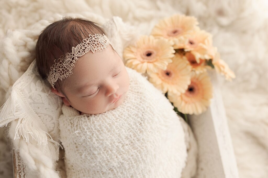 newborn baby wrapped in cream laying next to flowers Portland Doulas
