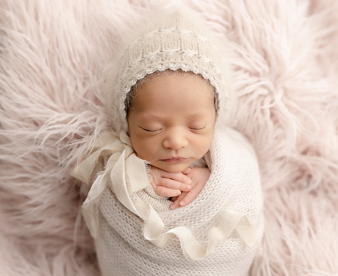 newborn baby in neutral wrap and hat laying on a pink fur blanket Two Rivers Midwifery