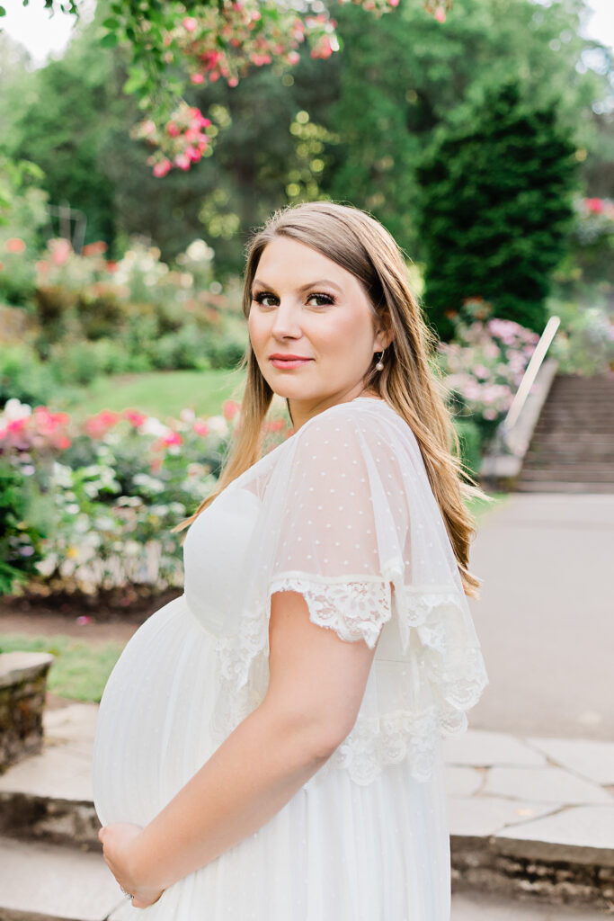 mom to be in white maternity gown holding her bump in a garden