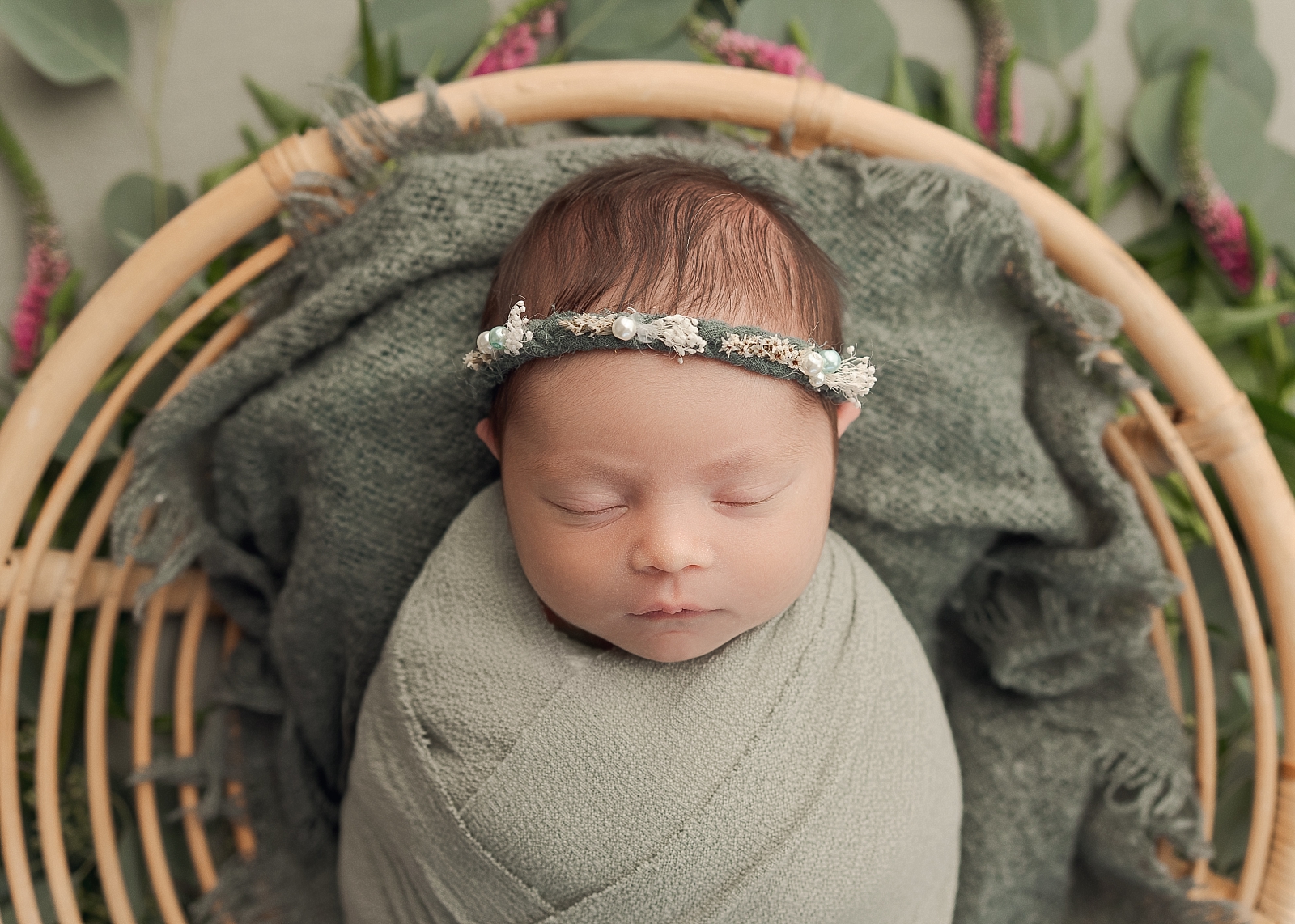 newborn baby girl wrapped in green with a headband laying in a basket