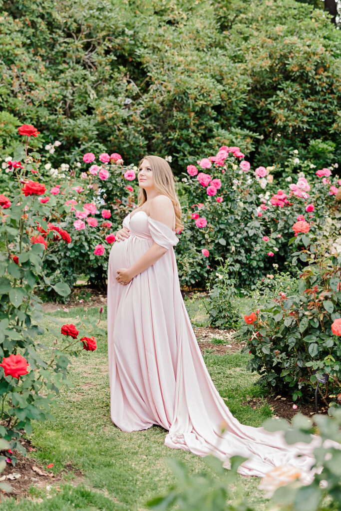 mom to be in pink maternity gown standing in a garden maternity clothes portland