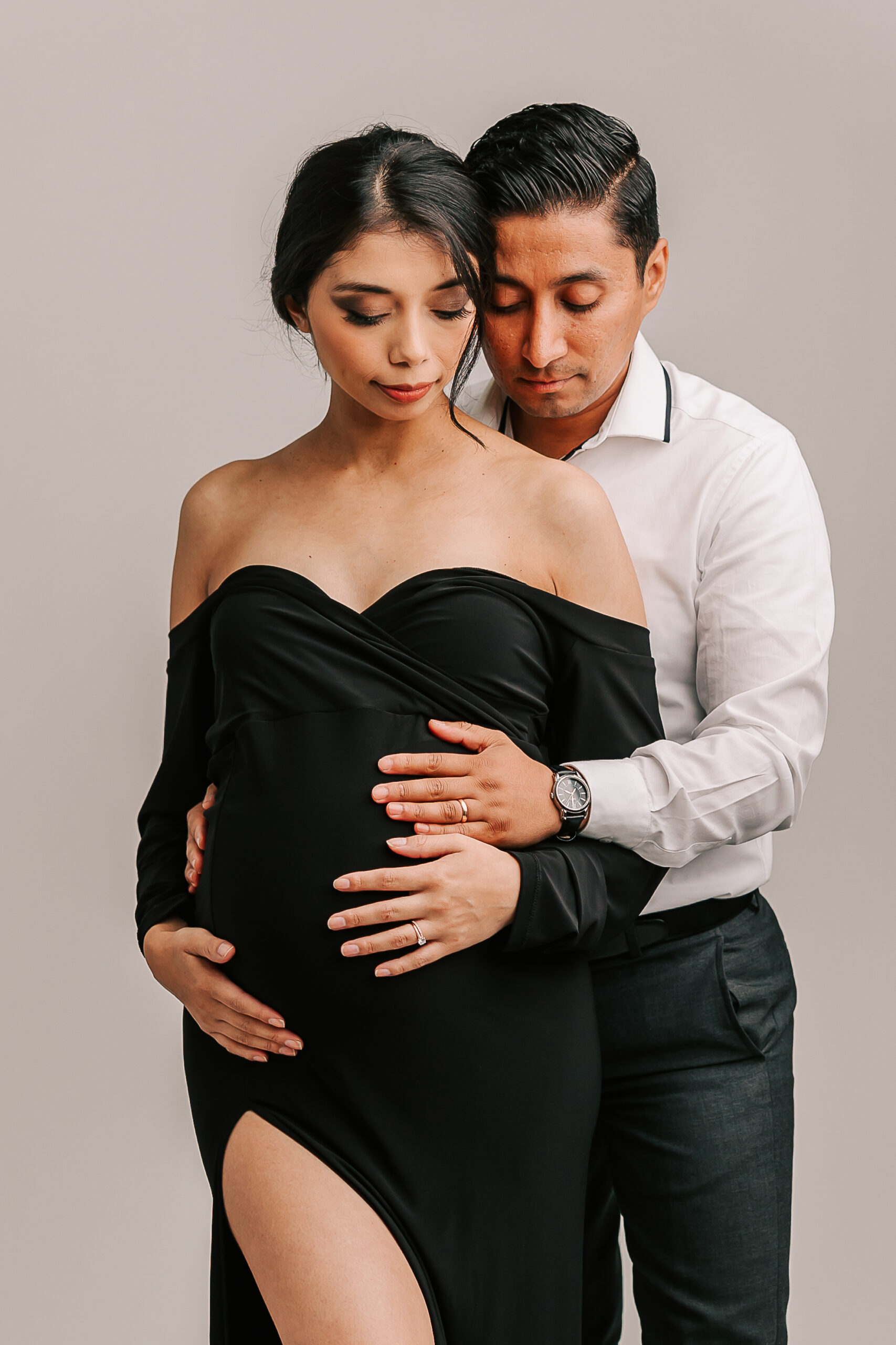 dad to be holding his wife's baby bump from behind