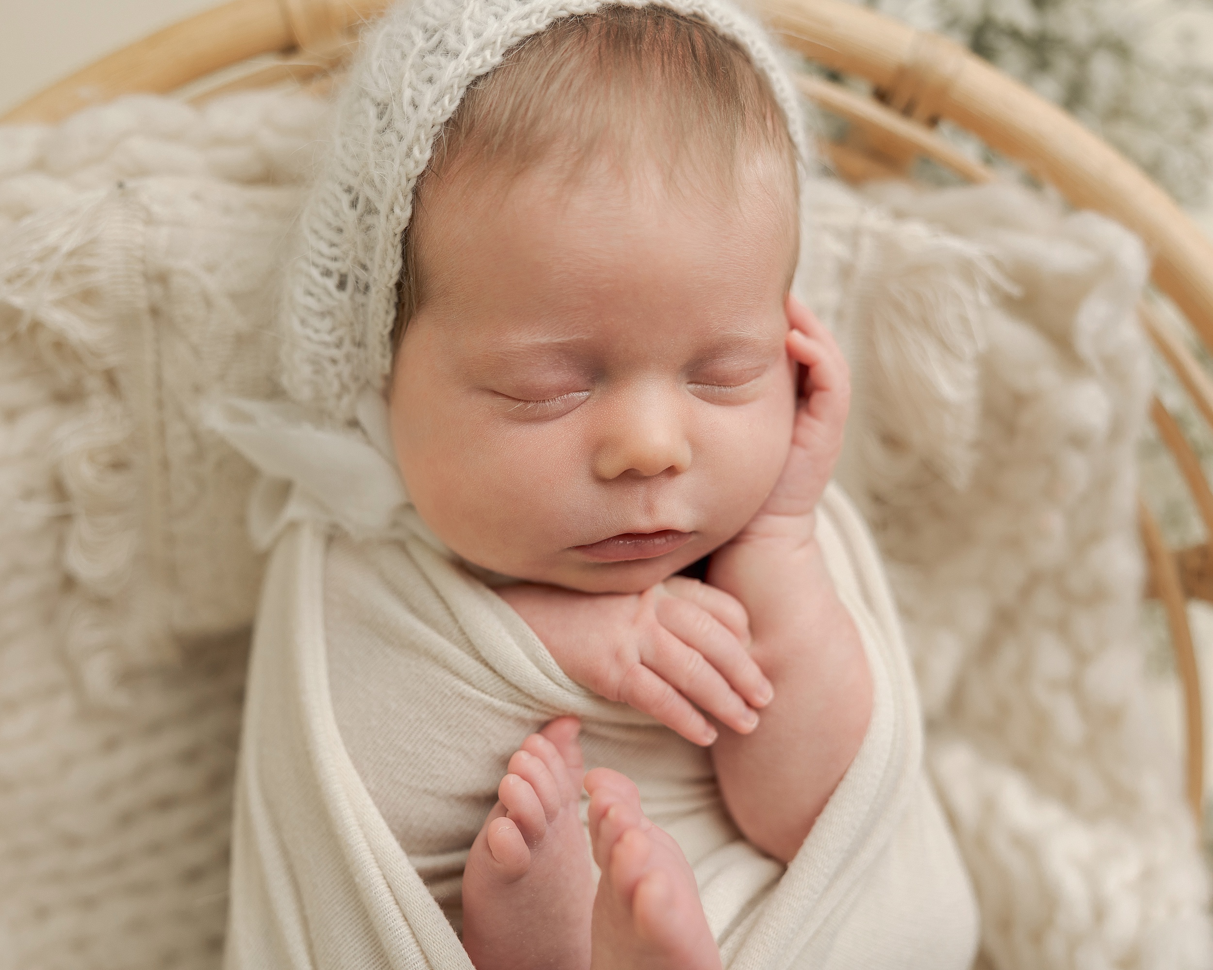 newborn baby wrapped in neutral colors sleeping with their hands on their face Rosehip Midwifery