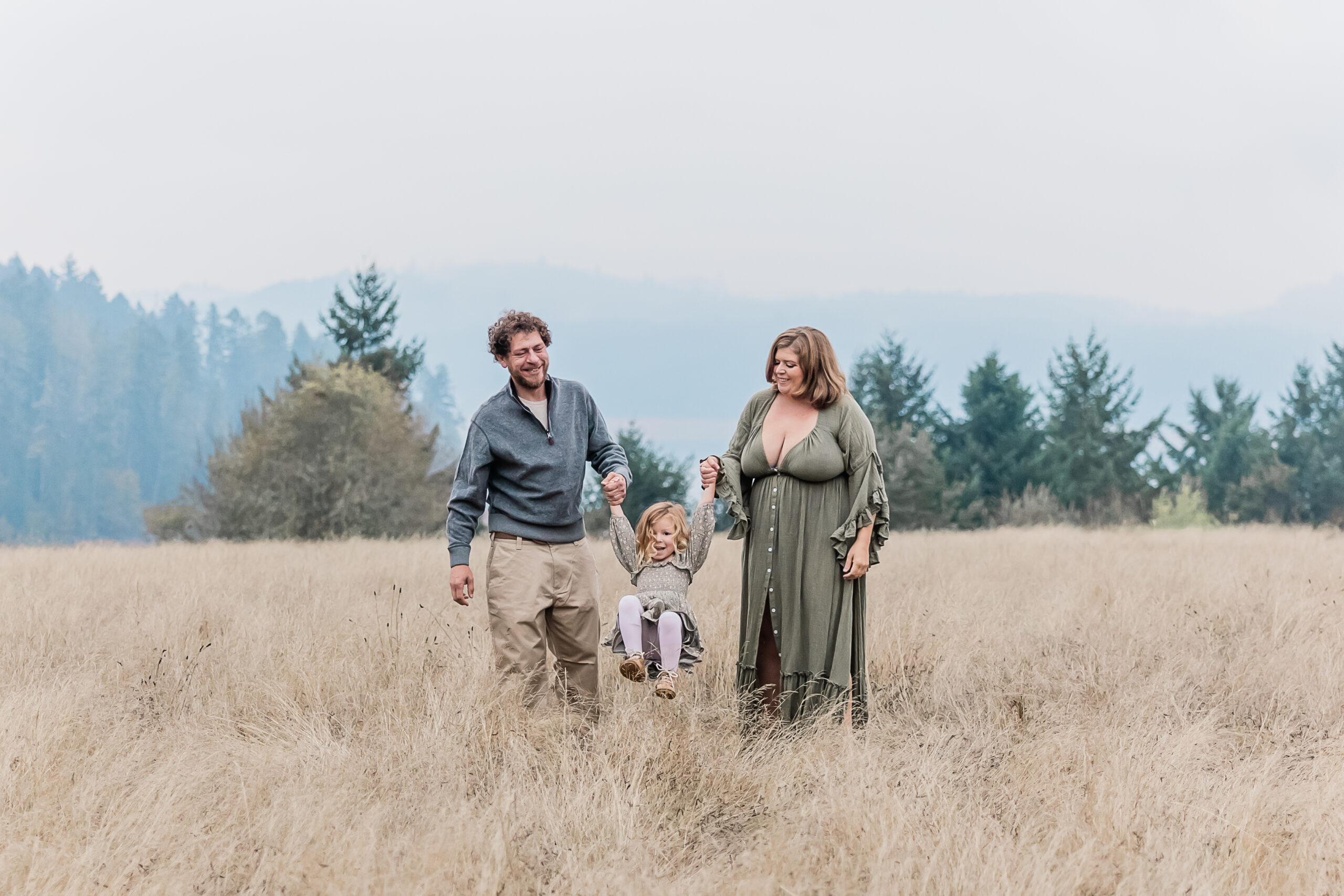 mom and dad swinging their little girl between them in an open field near portland