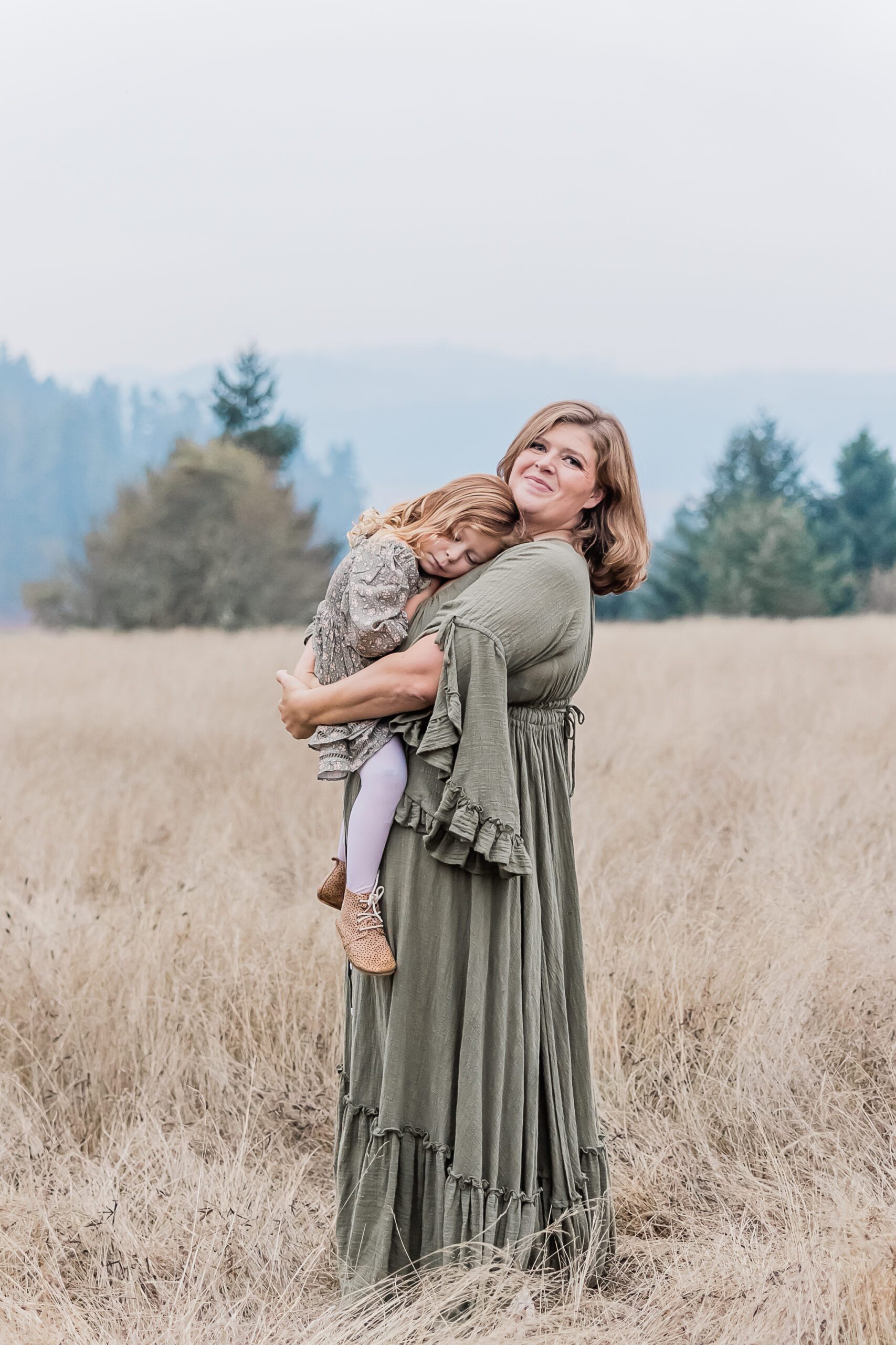 mom holding on to her young daughter in a field near portland yoga studios