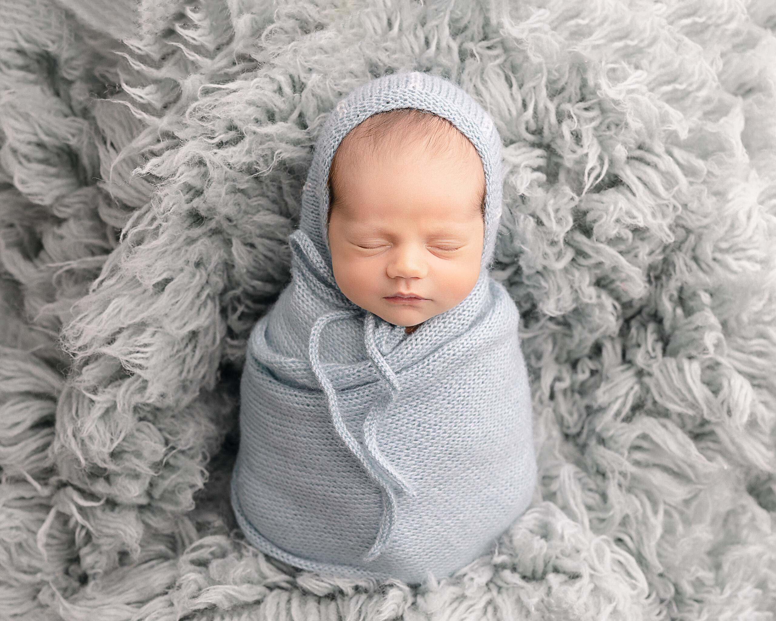 newborn baby wrapped in light blue laying on a grey blanket Northwest Community Midwives