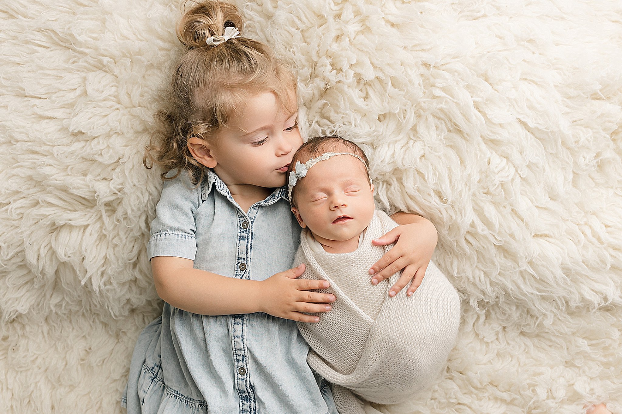 little girl kissing her newborn sister on the head